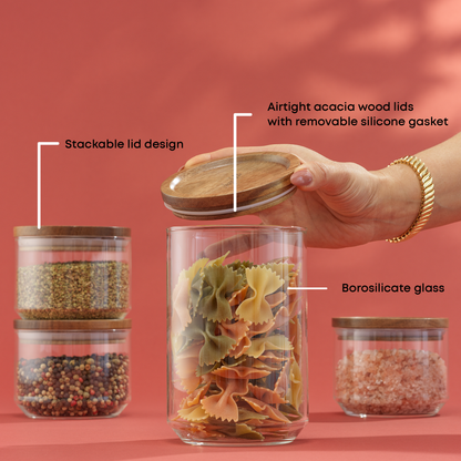 Glass storage jars with wooden lids, filled with various foods, on a red background. With text: "borosilicate glass, stackable lid design, airtight acacia wood lids with removable silicone gasket"