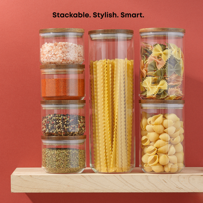 Stackable glass jars with various pasta and spices on a wooden shelf against a red background.