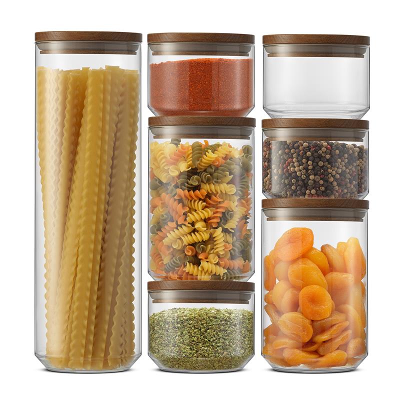 Set of glass storage jars with wooden lids containing various dry goods on a white background
