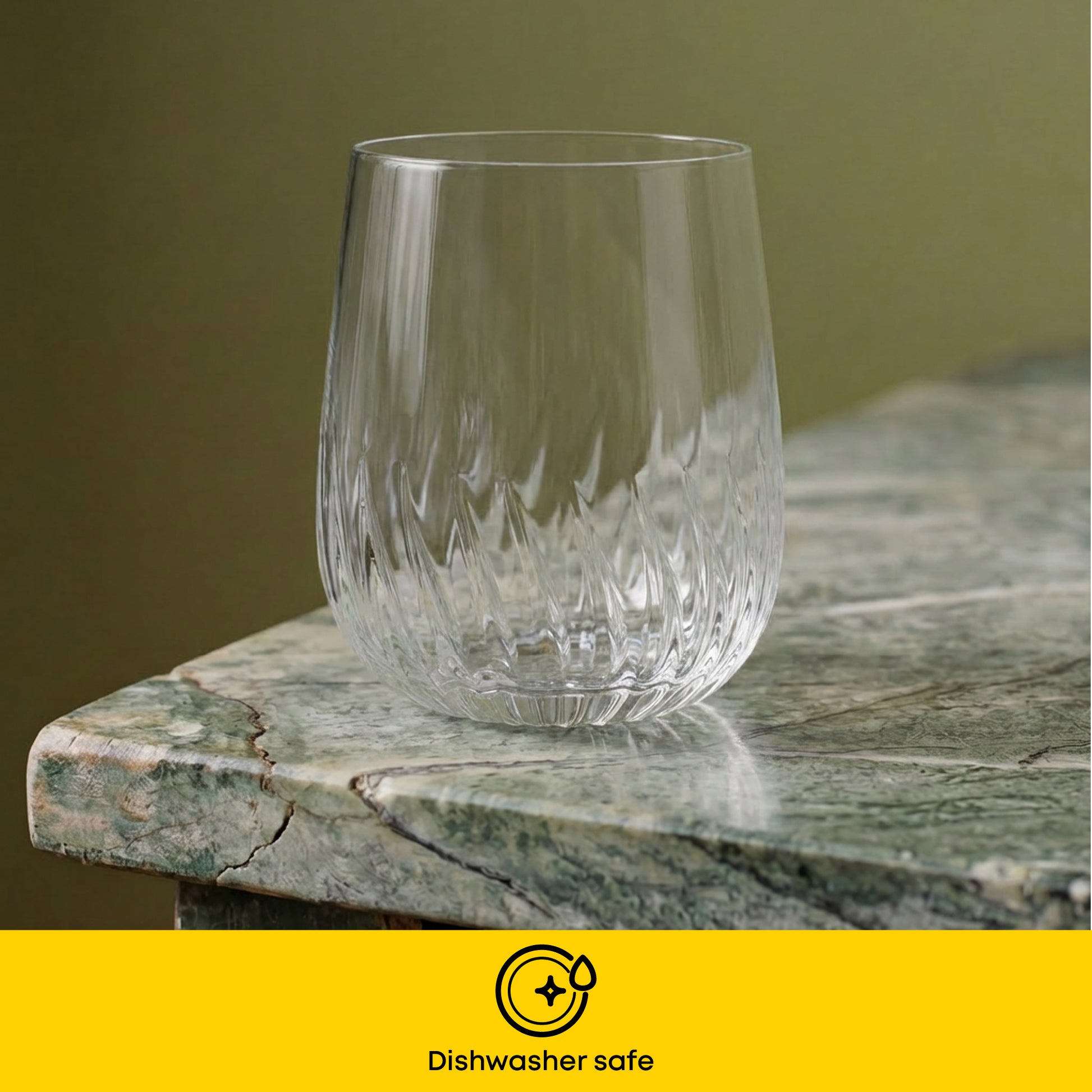 A clear cut-crystal glass with a textured wavy pattern, shown on a green marble surface with a yellow banner at the bottom reading 'Dishwasher safe'.