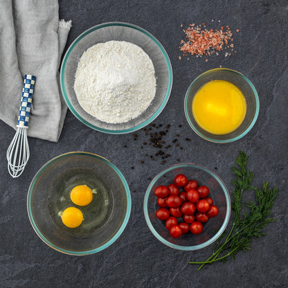 Top down shot of glass bowls full of eggs, tomatoes, and flour on a granite countertop